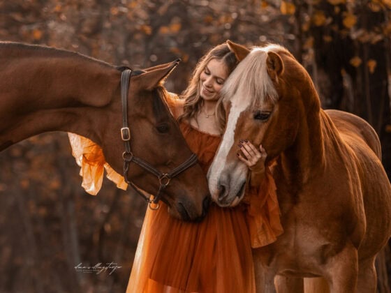 Carina Auer umarmt liebevoll ihre beiden Pferde Aquarell und Pop Up in einer herbstlichen Waldkulisse. ©️ Carina Auer / Elena Willingstorfer