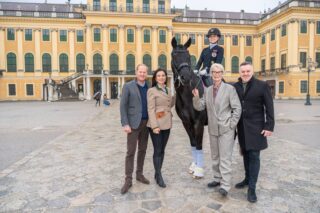 Reiterin auf Pferd mit Begleitern vor Schloss in Wien.