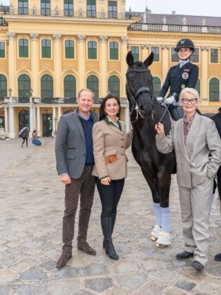 Reiterin auf Pferd mit Begleitern vor Schloss in Wien.